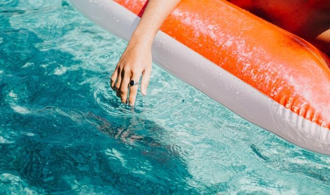 woman dangles her hand in the pool as she floats in an inflatable vessel